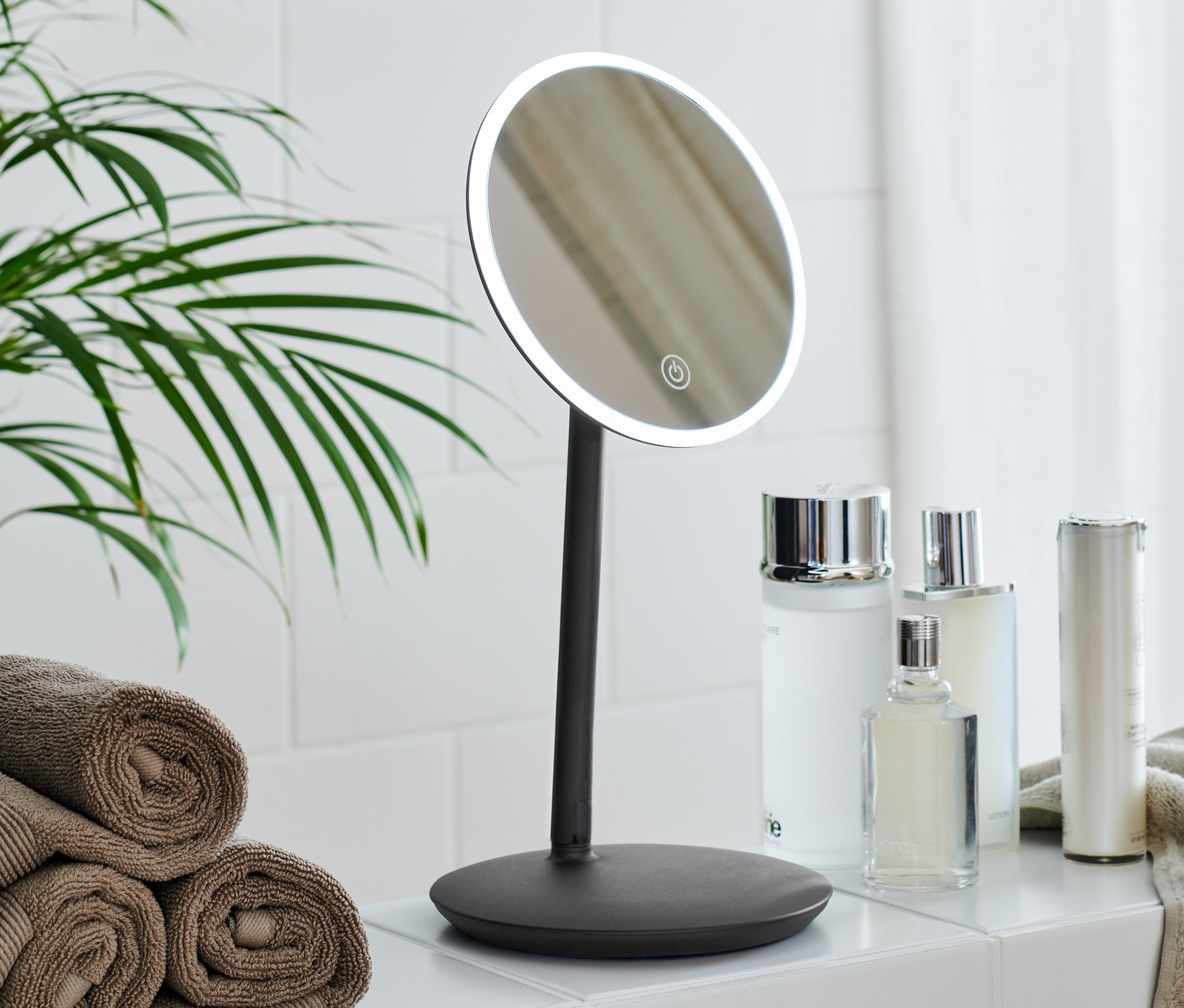 LED makyaj aynası, kozmetik ürünleri ve havlu yığını olan banyo.