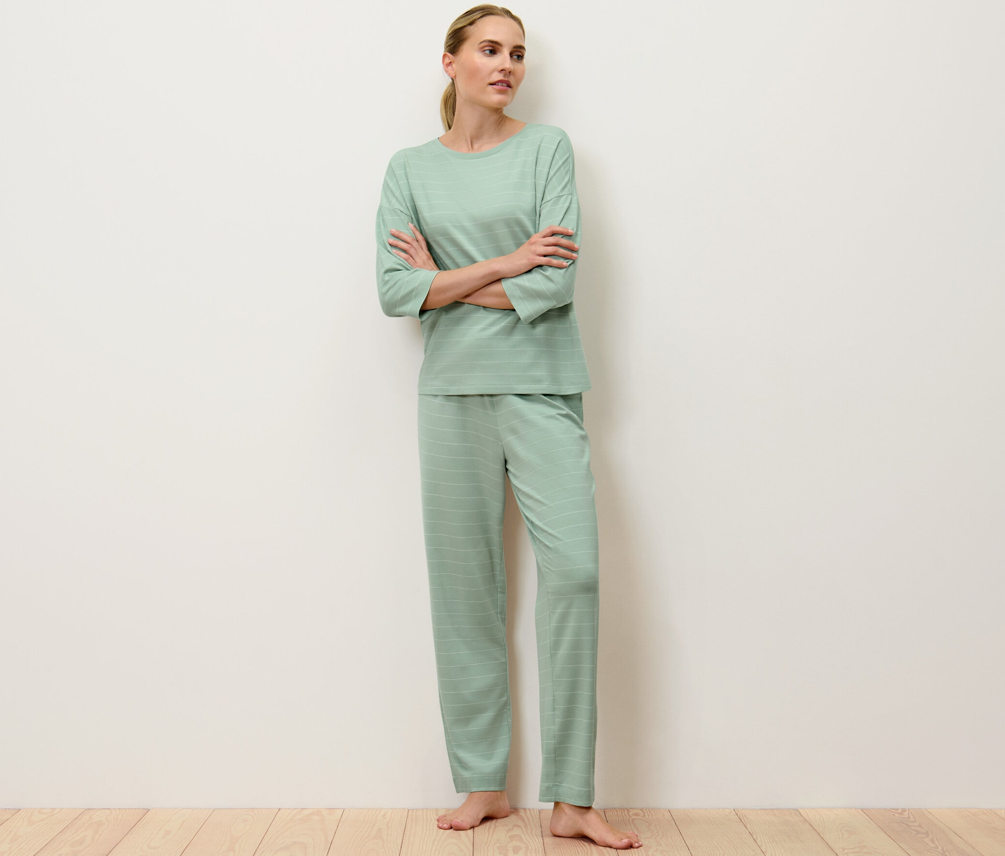 Kadın kolları kavuşturmuş, açık yeşil çizgili bir pijama giyiyor.