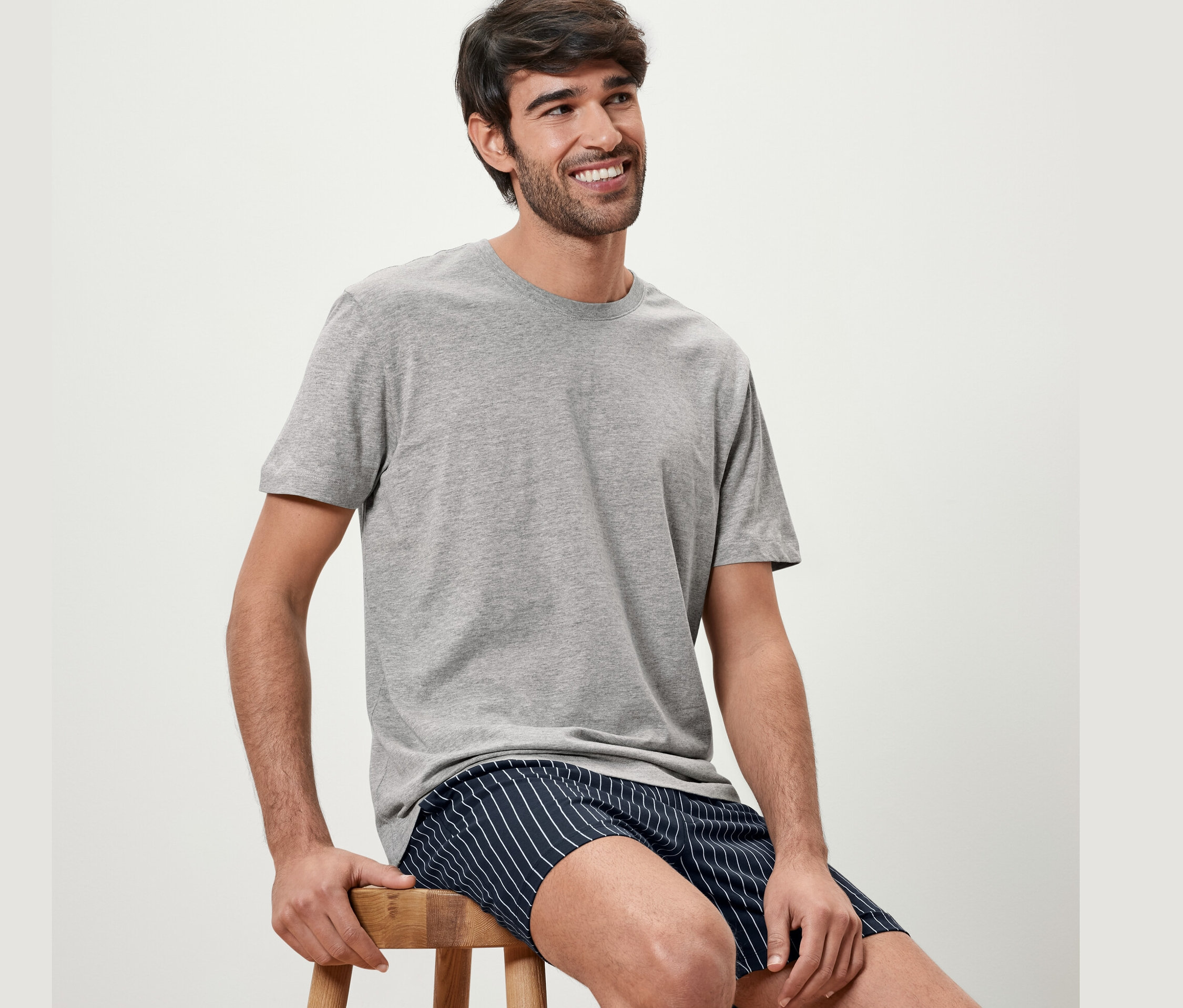 Adam sandalyede oturuyor, gri şortlu pijama takımı giyiyor.