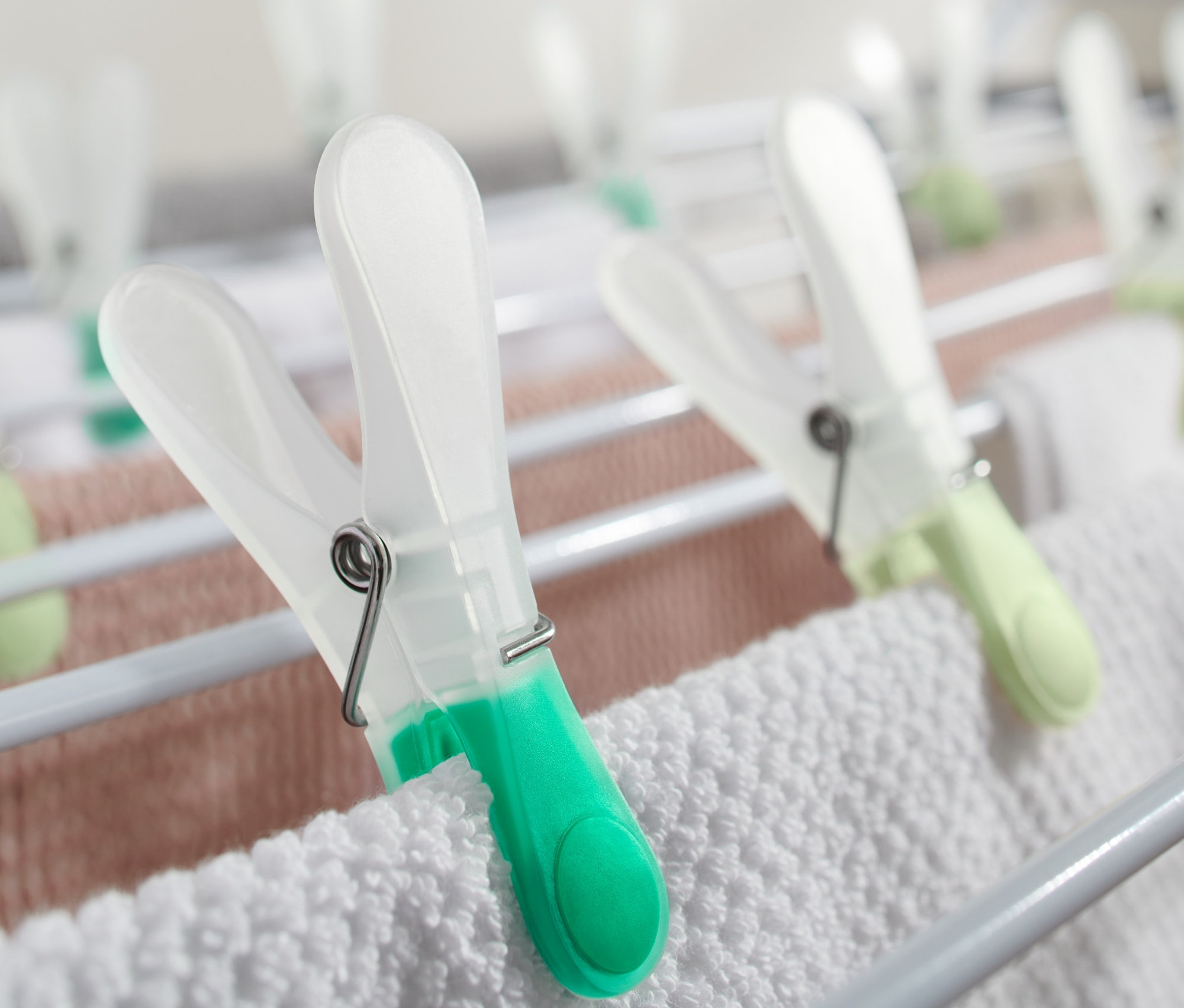 Çamaşır kurutma askısında beyaz ve pembe havluları tutan 20 adet çamaşır mandalının yakın çekimi.