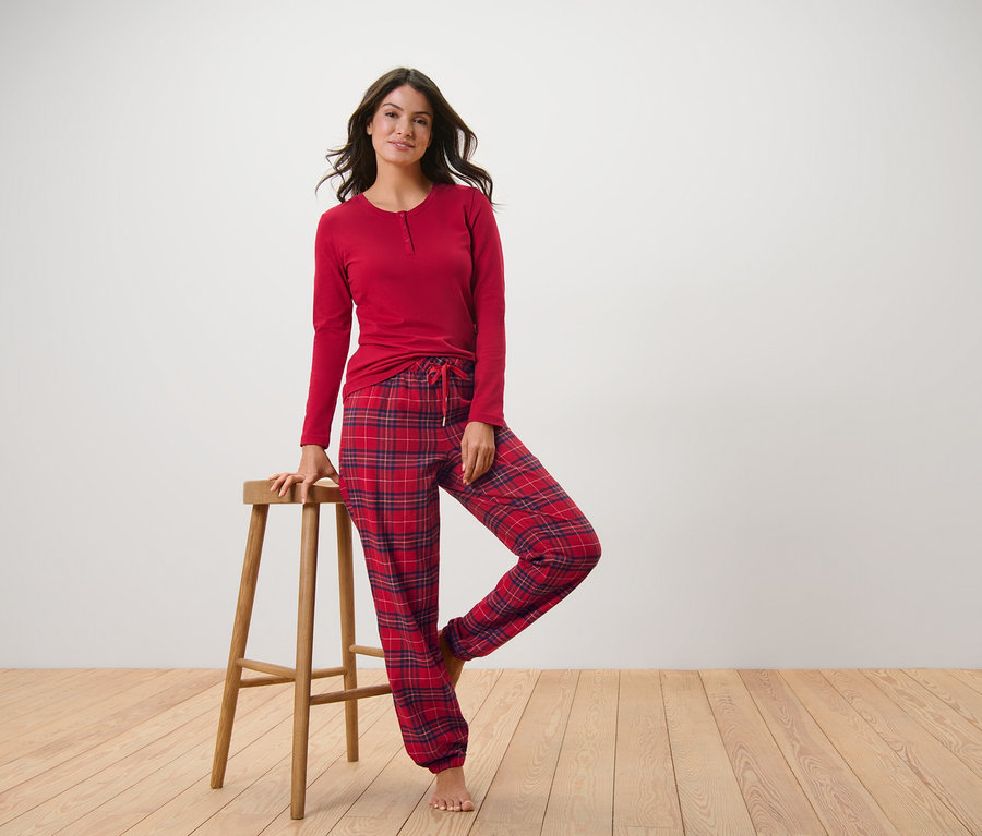 Kadın, kırmızı kareli flanel pijamasıyla poz veriyor, bir eli ahşap taburede.