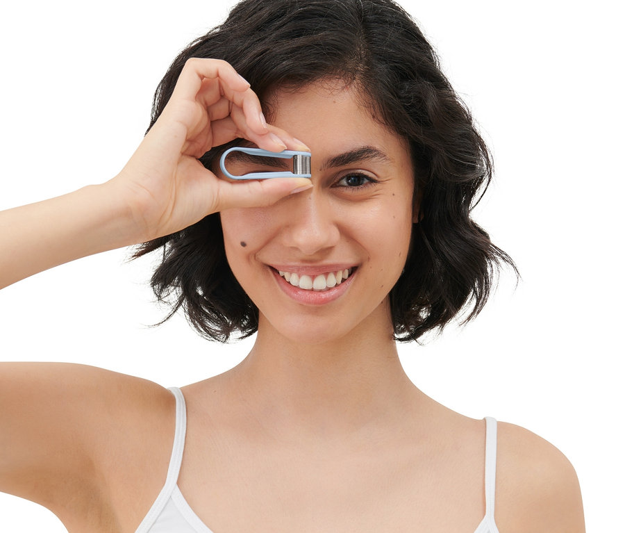 Kadın gülümsüyor ve gözünün önünde manuel bir mini yüz epilatörü tutuyor.