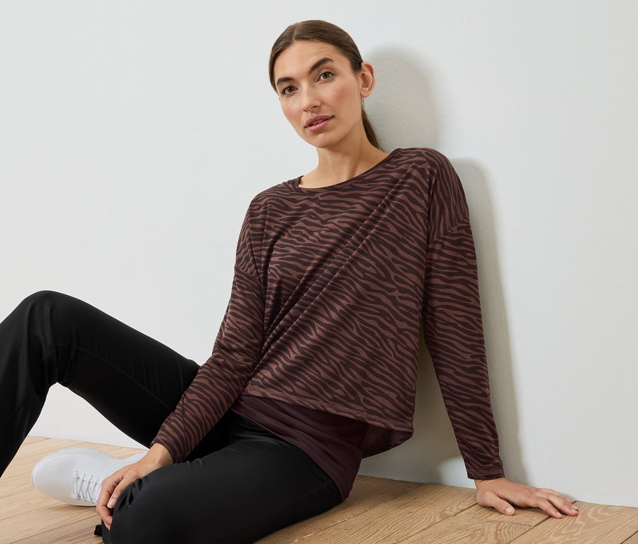 Kadın yerde oturuyor, kahverengi-siyah zebra desenli bir üst ve siyah pantolon giyiyor.