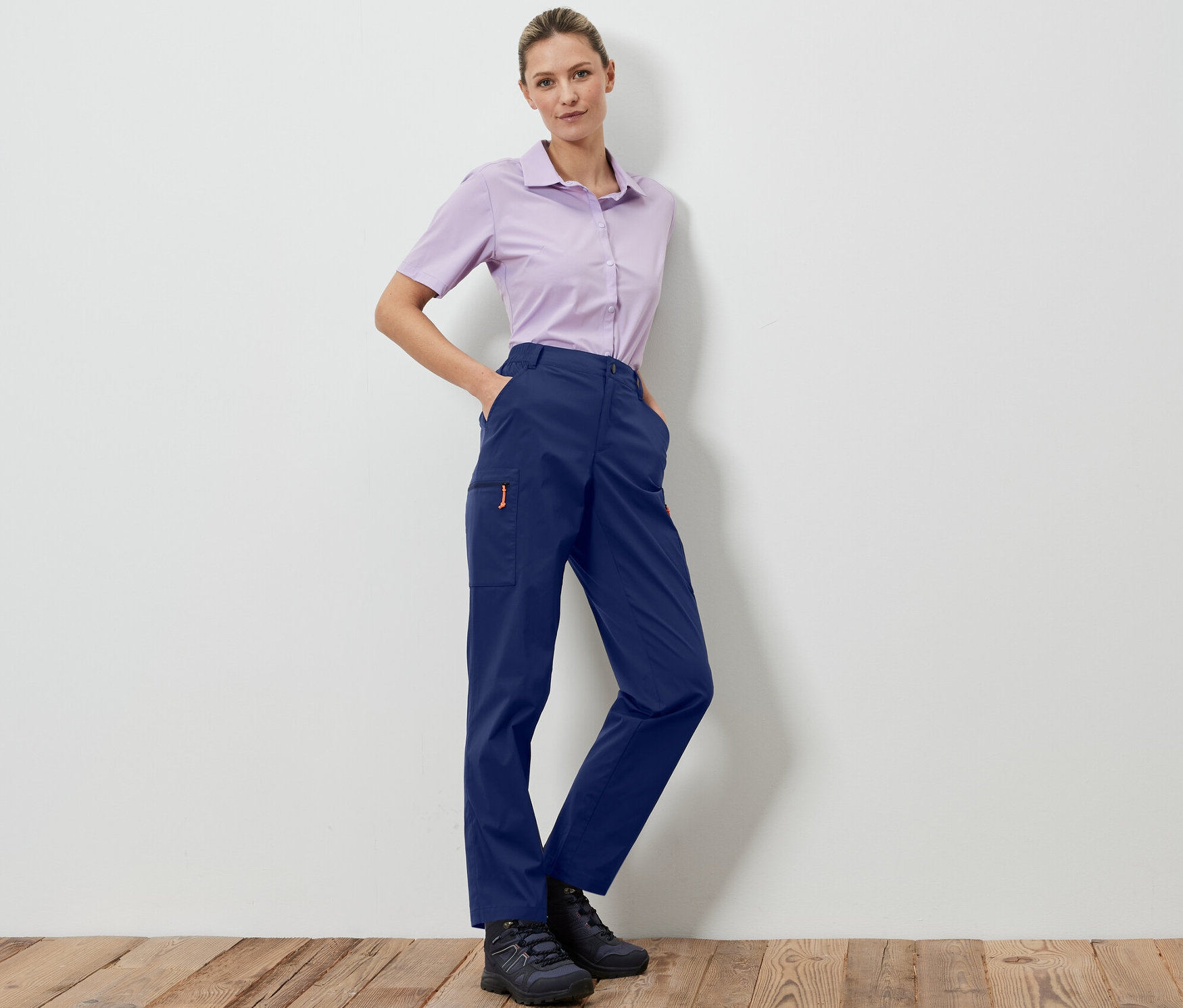 Bir kadın lacivert, kendi cebine toplanabilir outdoor pantolonu ve açık lila gömleğiyle poz veriyor.
