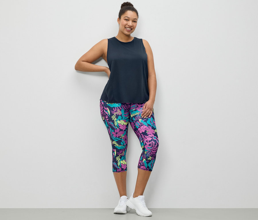 Kadın, lacivert bir spor atlet ve tamamı baskılı 3/4 spor tayt ile poz veriyor.