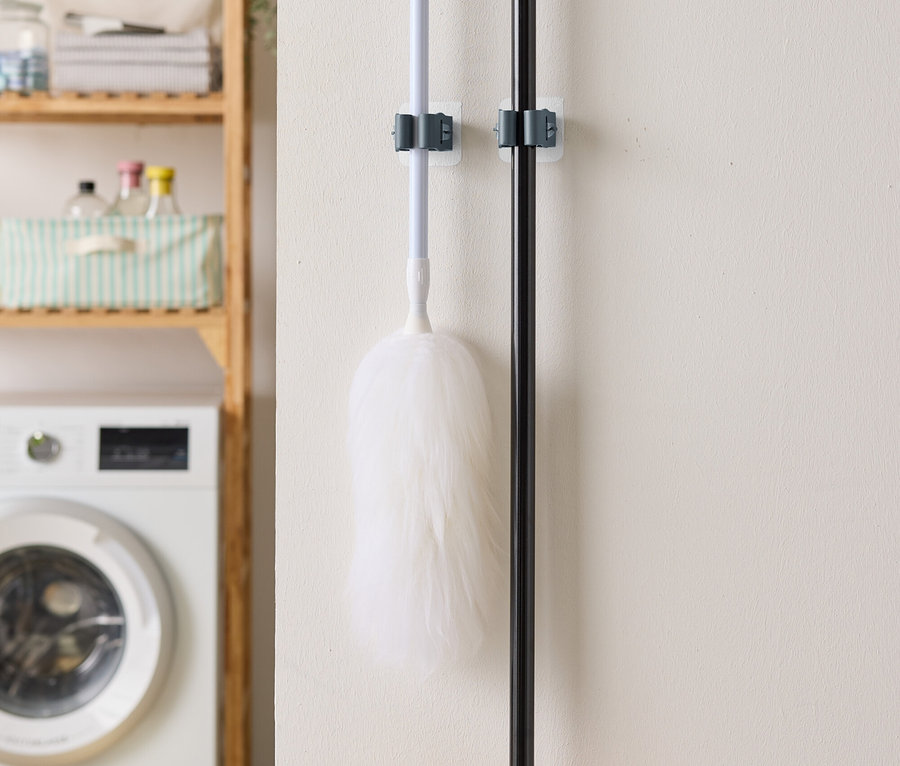 Duvara asılı bir toz bezi ve süpürge, arka planda bir çamaşır makinesi ve raf.