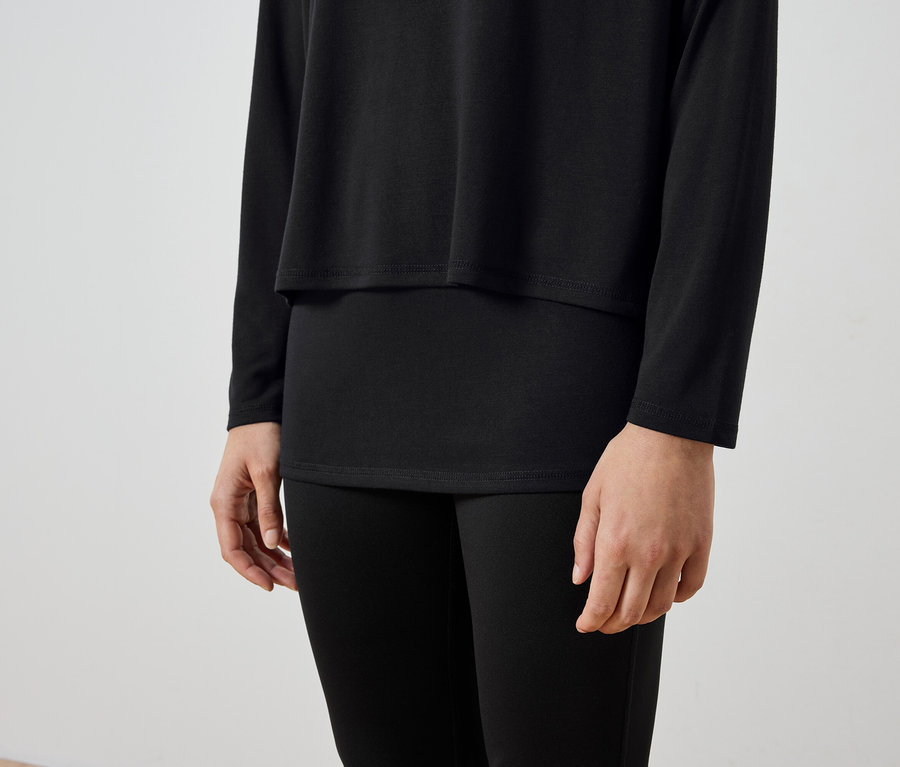 Siyah uzun kollu tişört ve siyah tayt giyen bir kişinin gövdesi.