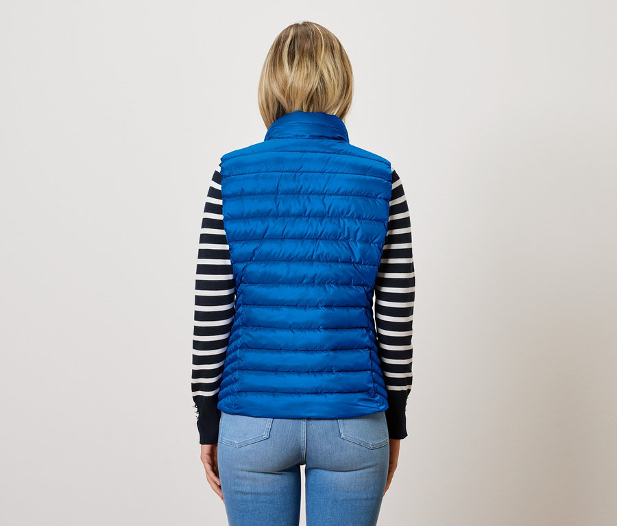 Sırtı dönük bir kadın, çizgili bir kazağın üzerinde mavi, kapitone bir yelek giyiyor.