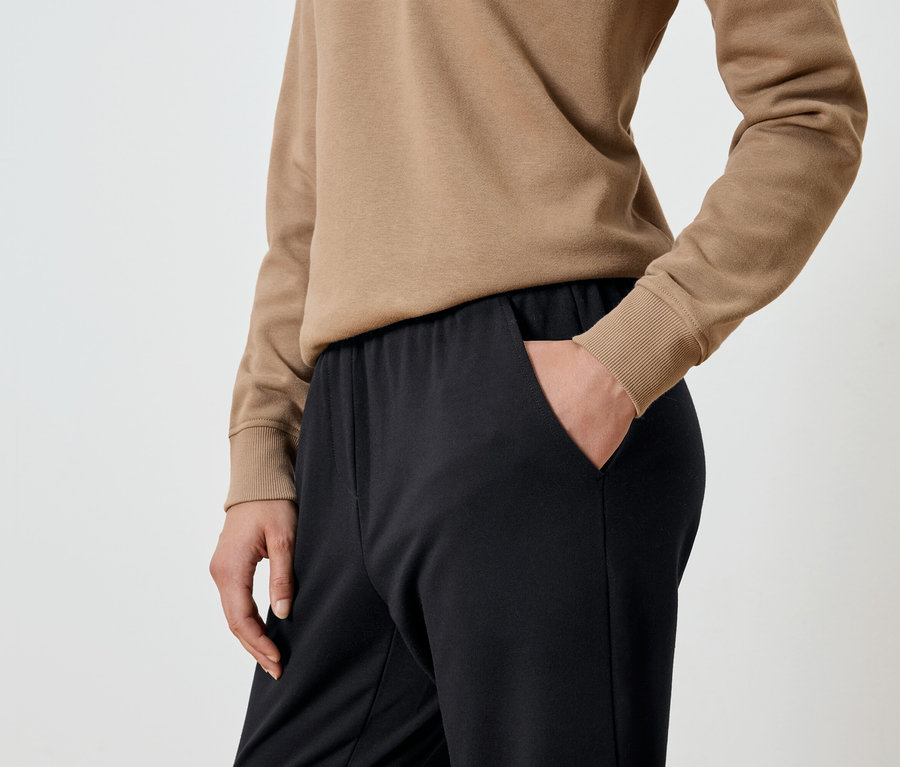 Eliyle siyah eşofmanının cebine sokulmuş bej rengi sweatshirt'lü bir kadın detayı.
