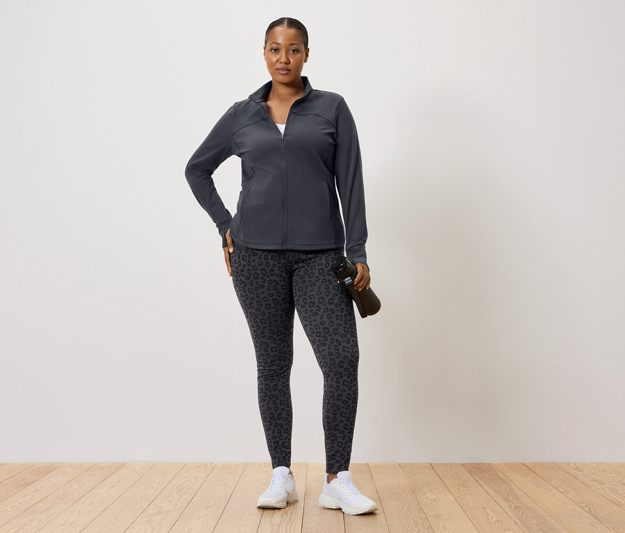 Koyu renk spor ceket ve leopar desenli tayt giyen, elinde su şişesi olan kadın.