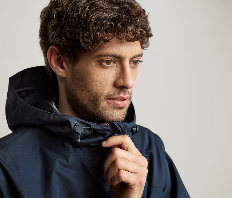 Kıvırcık saçlı bir adam kapüşonlu lacivert bir ceket giyiyor.