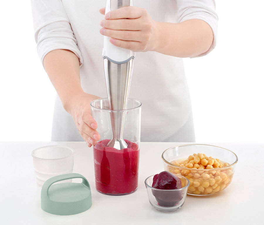 Kadın, bir karıştırma kabında smoothie yapıyor. Yanında taşınabilir yemek kutusu ve malzemelerle dolu kaseler var.
