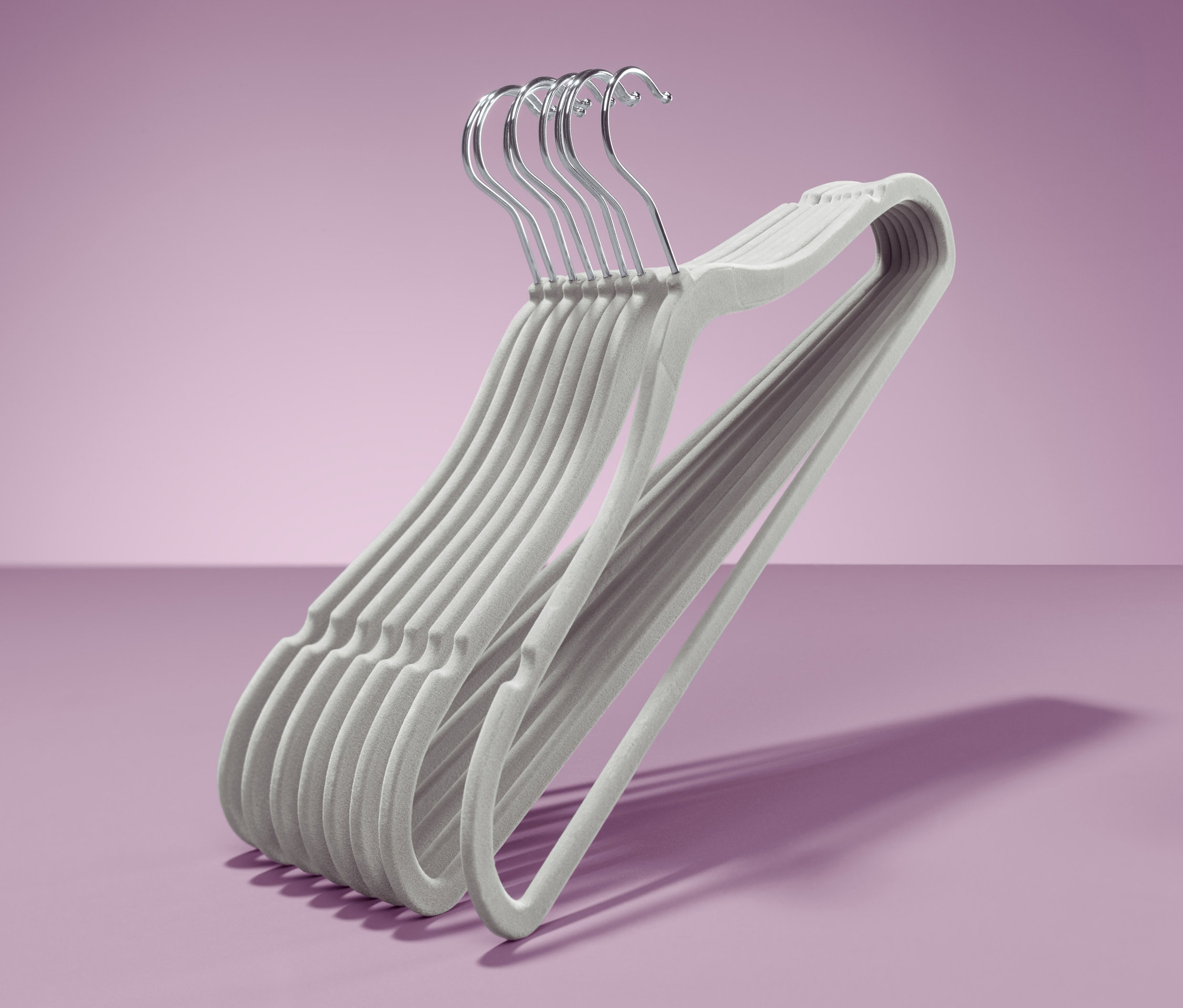 Sekiz adet ekstra ince kıyafet askısı mor bir zeminde üst üste duruyor.