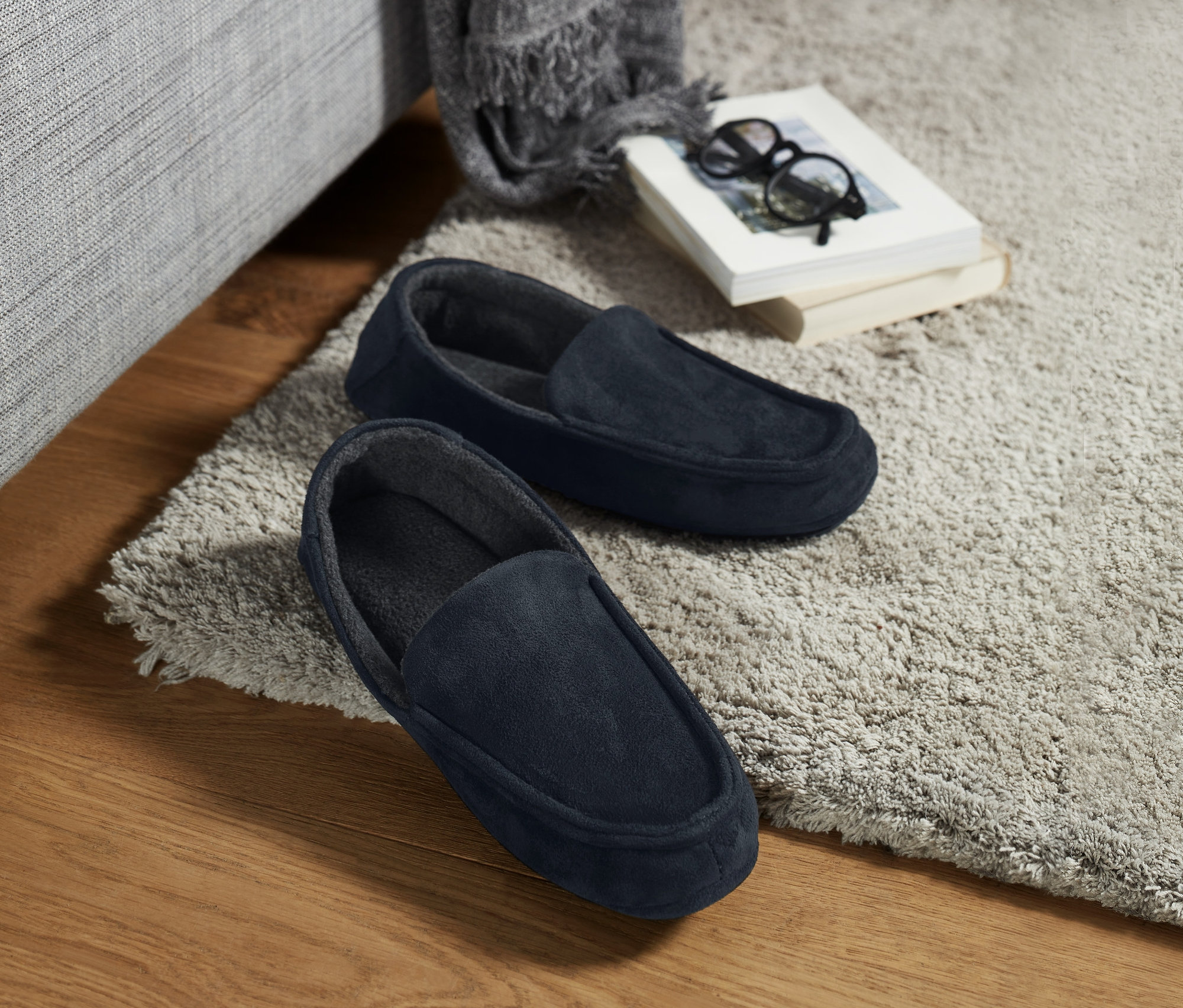 Bej halı üzerinde, kanepe yanında duran bir çift lacivert ev terliği.