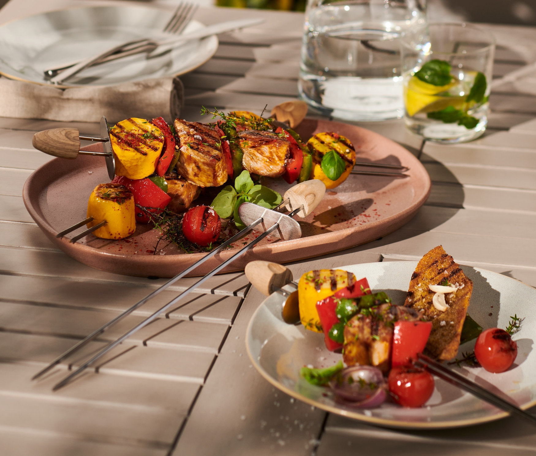 Ahşap bir masa üzerinde ızgara sebzeler ve et ile 4 adet şaşlık şişi bulunan iki tabak.