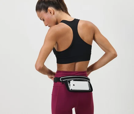 Kadın, beline Akıllı Telefon Koşu Kemerini ayarlıyor. Spor sutyeni ve tayt giyiyor.