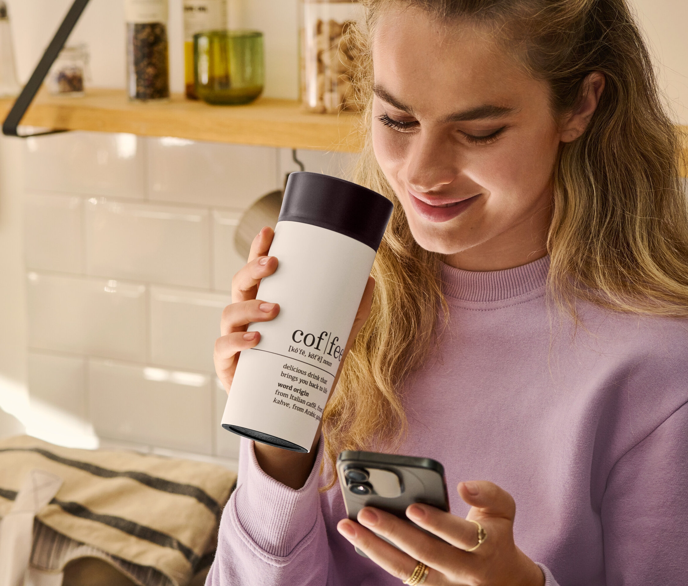 Kadın elinde Al-Götür Kahve Bardağı, Coffee Dictionary tutuyor ve cep telefonuna bakıyor.