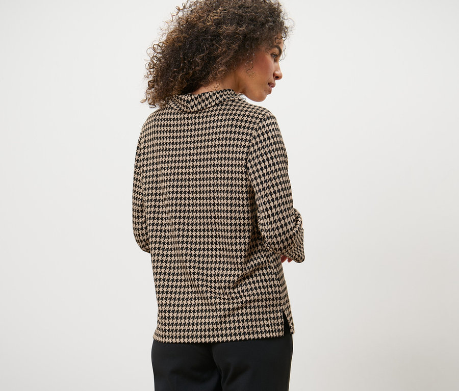 Kıvırcık saçlı bir kadının arkadan görünüşü. Kadın, 3/4 kollu, kazayağı desenli bir sweatshirt giyiyor.