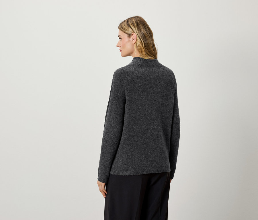 Kameraya arkası dönük bir kadın, koyu gri bir kazak ve siyah pantolon giyiyor.