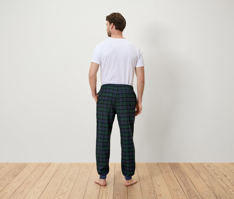 Arkası kameraya dönük bir adam beyaz tişört ve yeşil kareli pijama altı giyiyor.