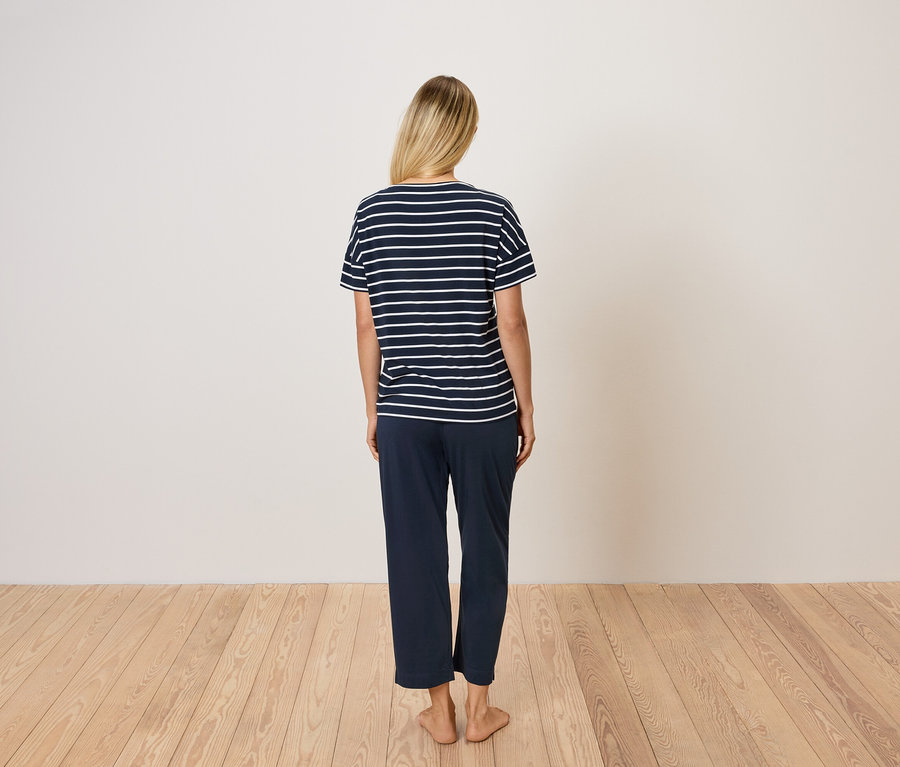 Arkadan görünüşüyle sarı saçlı, mavi çizgili tişört ve mavi pantolon giyen bir kadın.