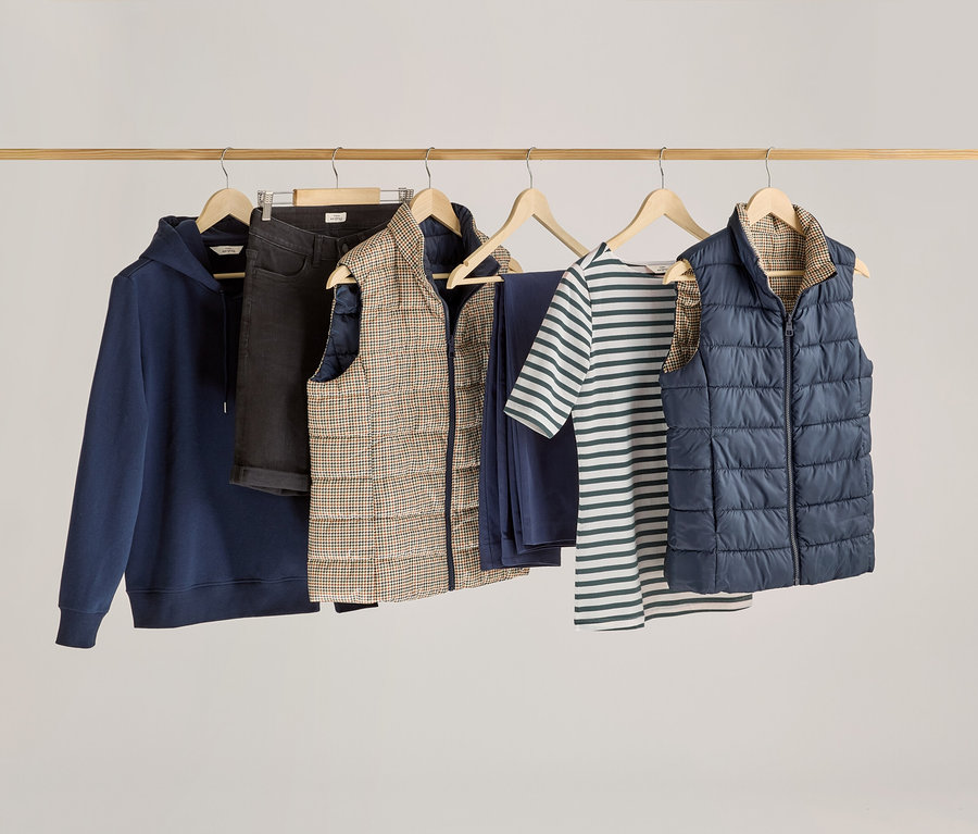 Giysiler ahşap bir çubuğa asılı, aralarında yeşil çizgili, yarım kollu bir tişört var.