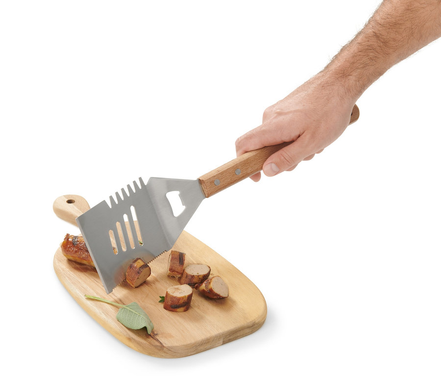 Bir el, kesilmiş sosisli bir ahşap kesme tahtasının üzerinde çok amaçlı bir BBQ aleti tutuyor.