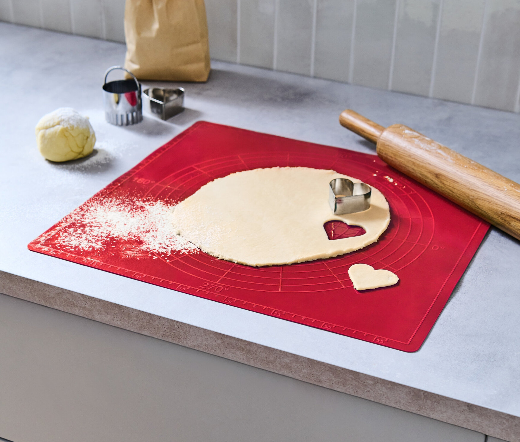 Hamur, kırmızı dayanıklı pişirme matı üzerinde kalp şeklinde kesiciyle açılıyor.