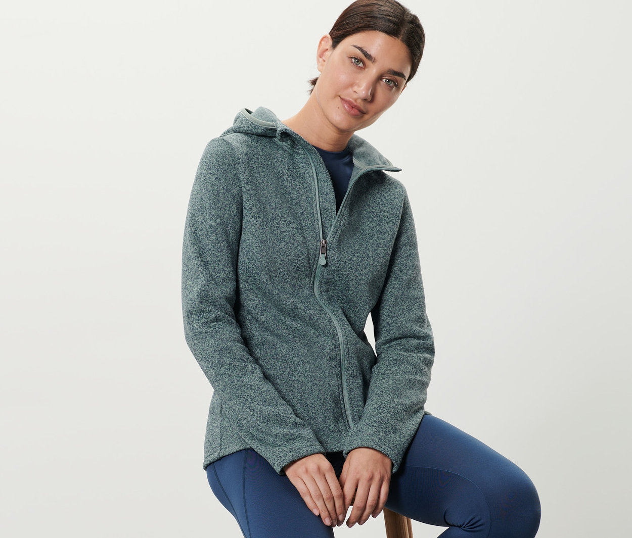 Bir kadın taburede oturuyor ve kırçıllı mint yeşili örgü polar ceket giyiyor.