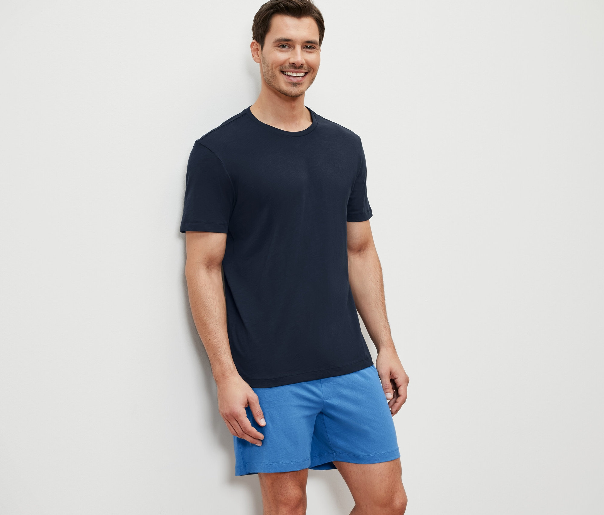 Bir adam Şortlu Pijama Takımı ile duvara yaslanmış gülüyor.