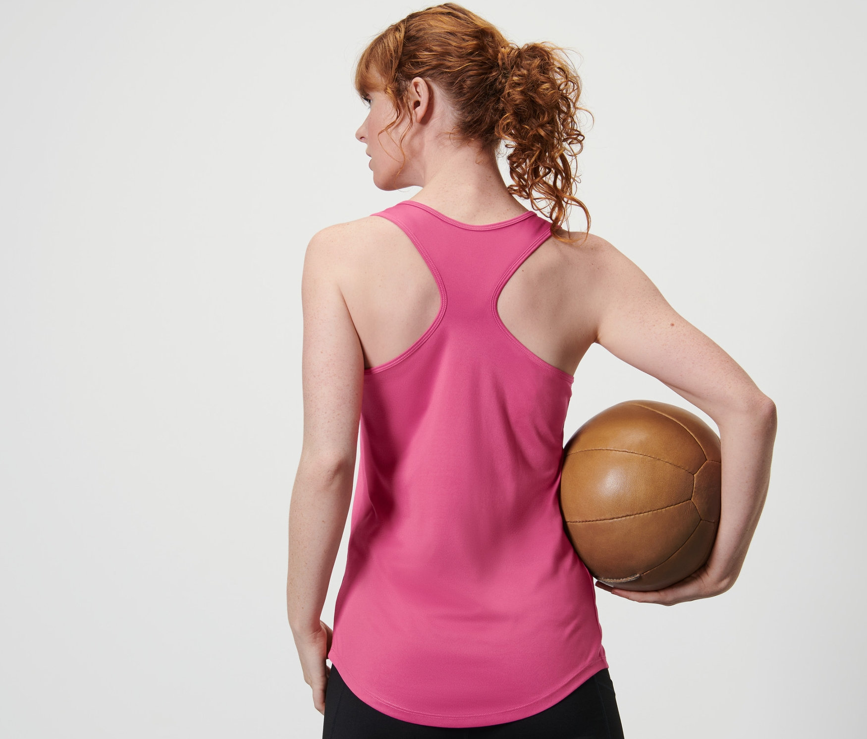Kadın arkadan iki parçalı bir setten pembe bir atlet ve siyah tayt içinde kahverengi bir top tutuyor.