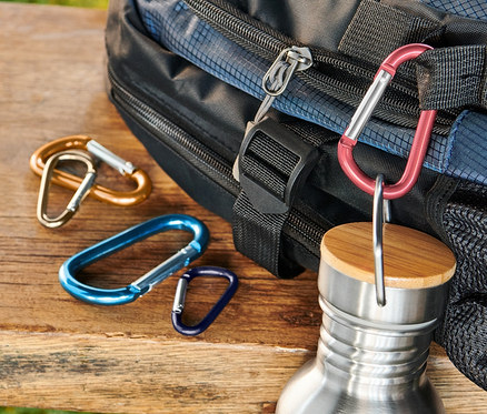 Mavi sırt çantası, paslanmaz çelik şişe ve 5 adet karabina ahşap bir bankın üzerinde duruyor.