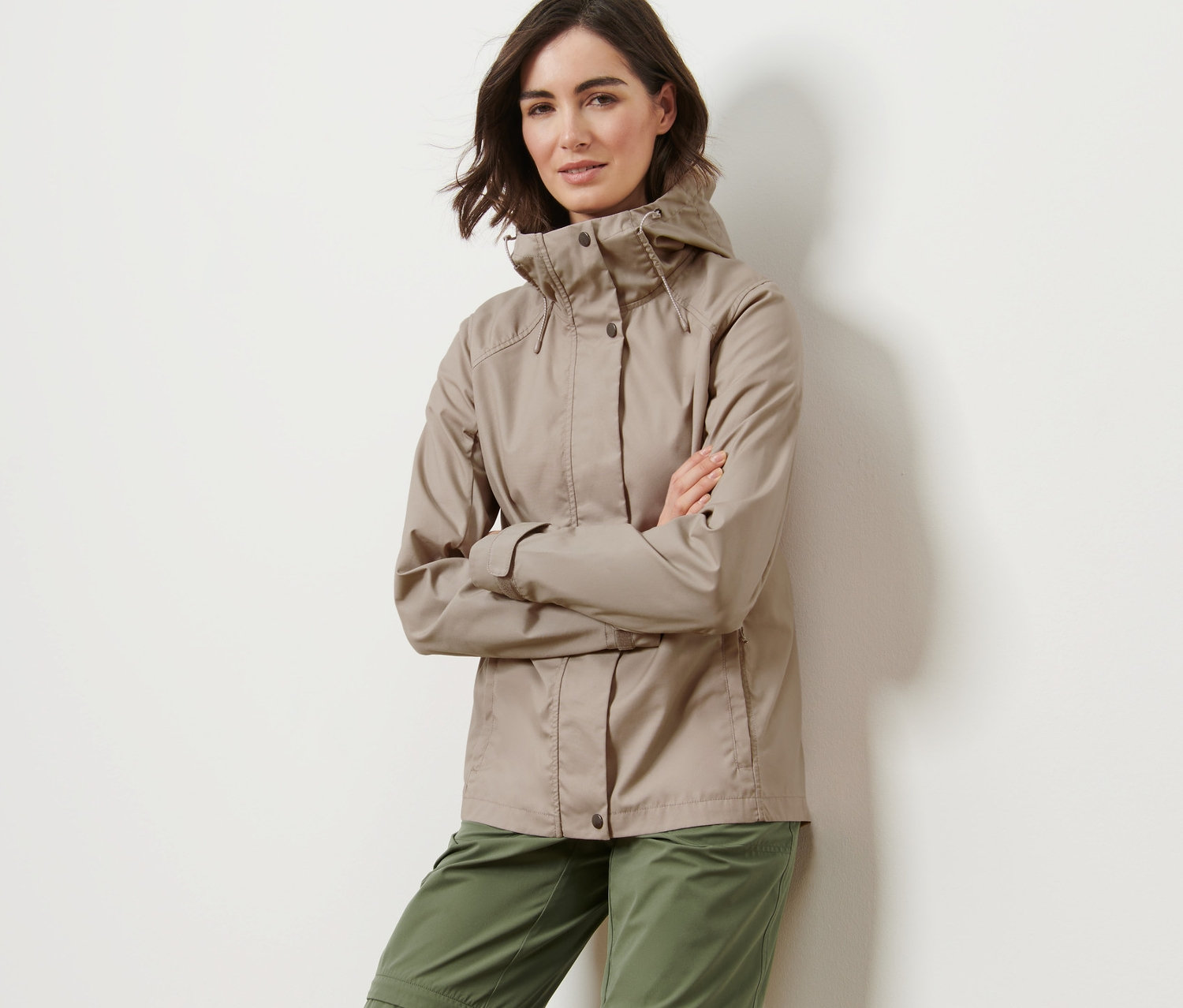 Kadın bej rengi Mevsimlik Ceket ve yeşil pantolonla poz veriyor.