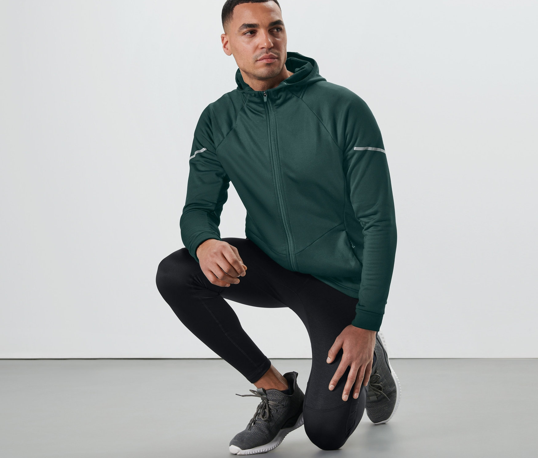 Koyu yeşil termal ceketli bir adam yerde diz çöküyor.