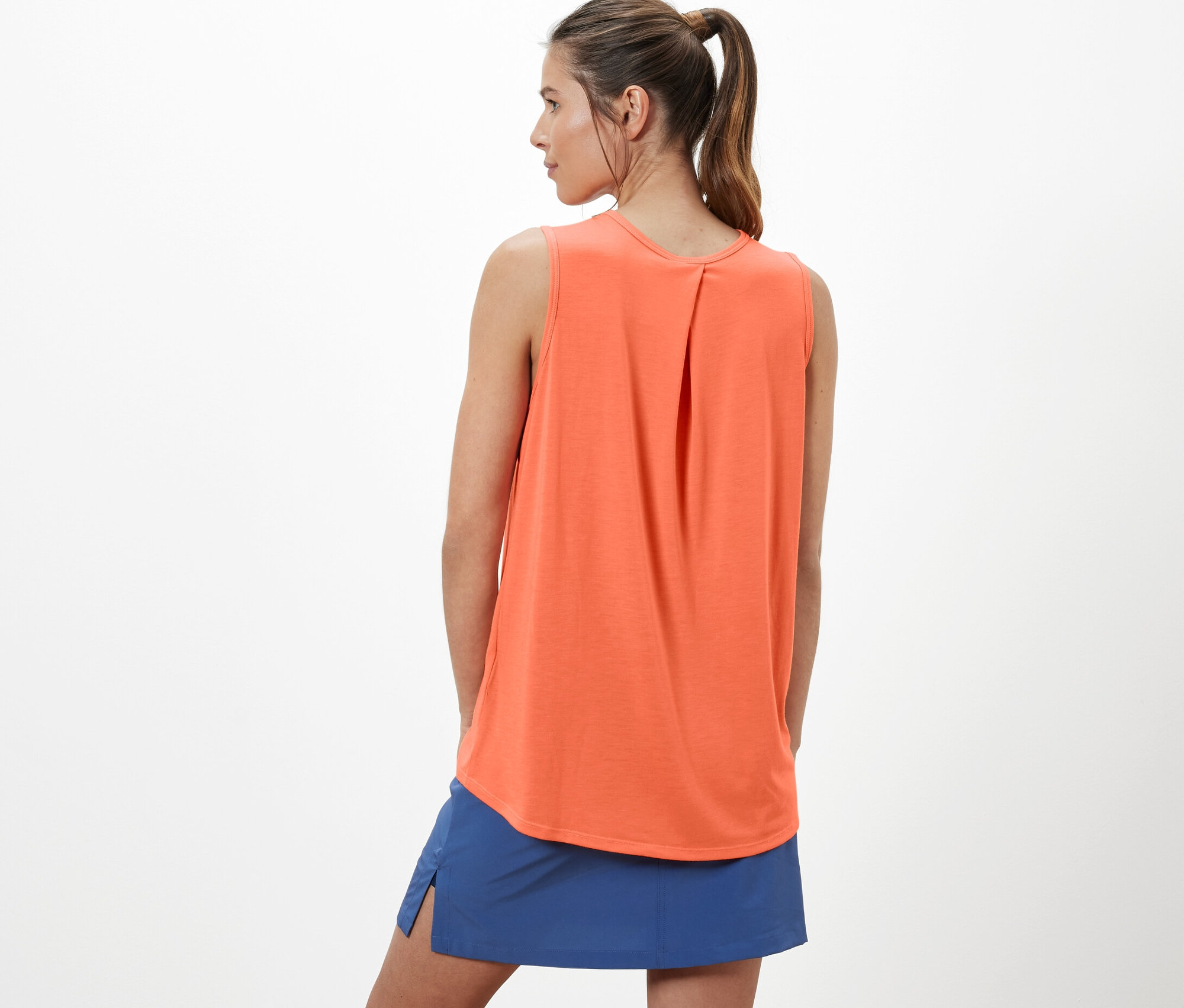 Kadın, turuncu bir outdoor fonksiyonel kolsuz tişört ve mavi bir etek giyiyor.