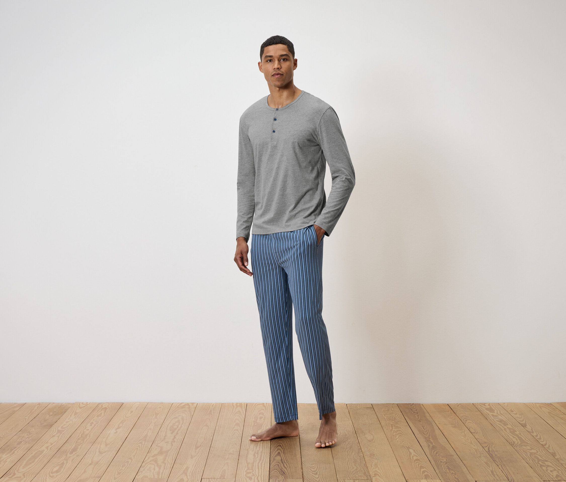 Adam yerde duruyor, üzerinde gri uzun kollu bir tişört ve mavi çizgili bir pantolon var.