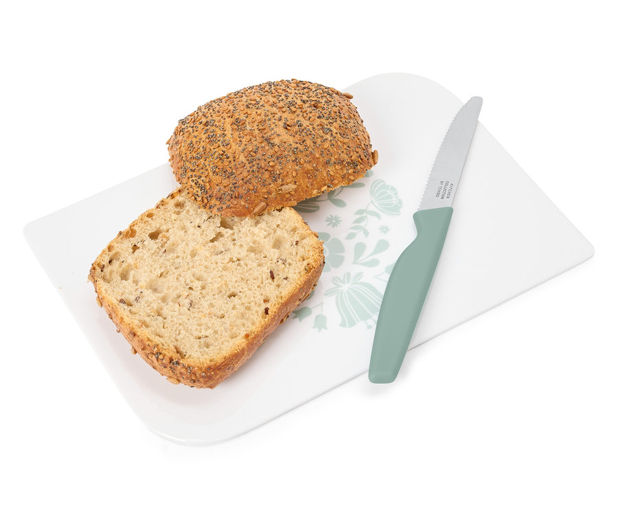 Çiçek desenli beyaz bir tahtanın üzerinde, yeşil bir bıçağın yanında bir dilim ve bütün bir somun ekmek duruyor.