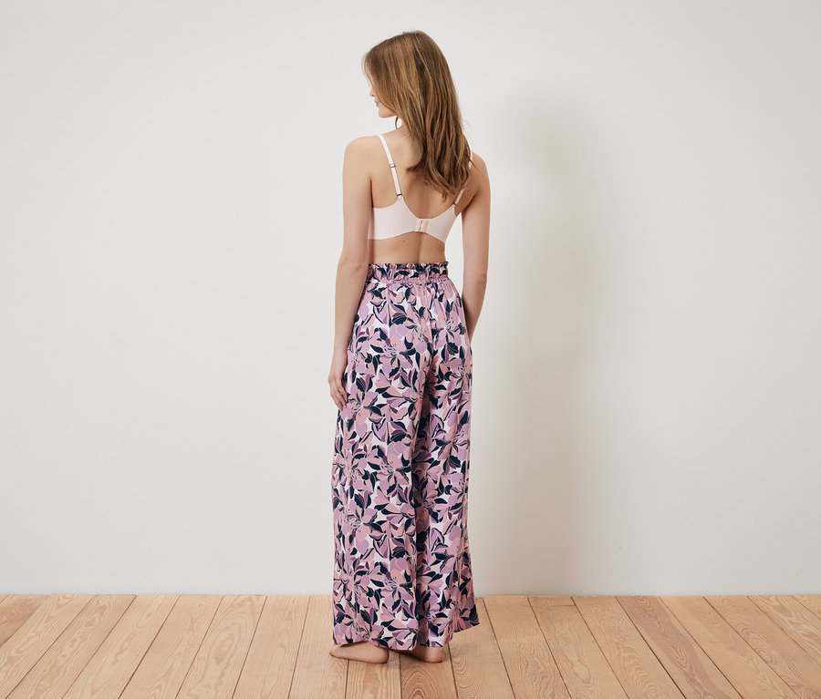 Arkası dönük bir kadın pembe sütyen ve çiçek desenli, bol bir pantolon giyiyor.