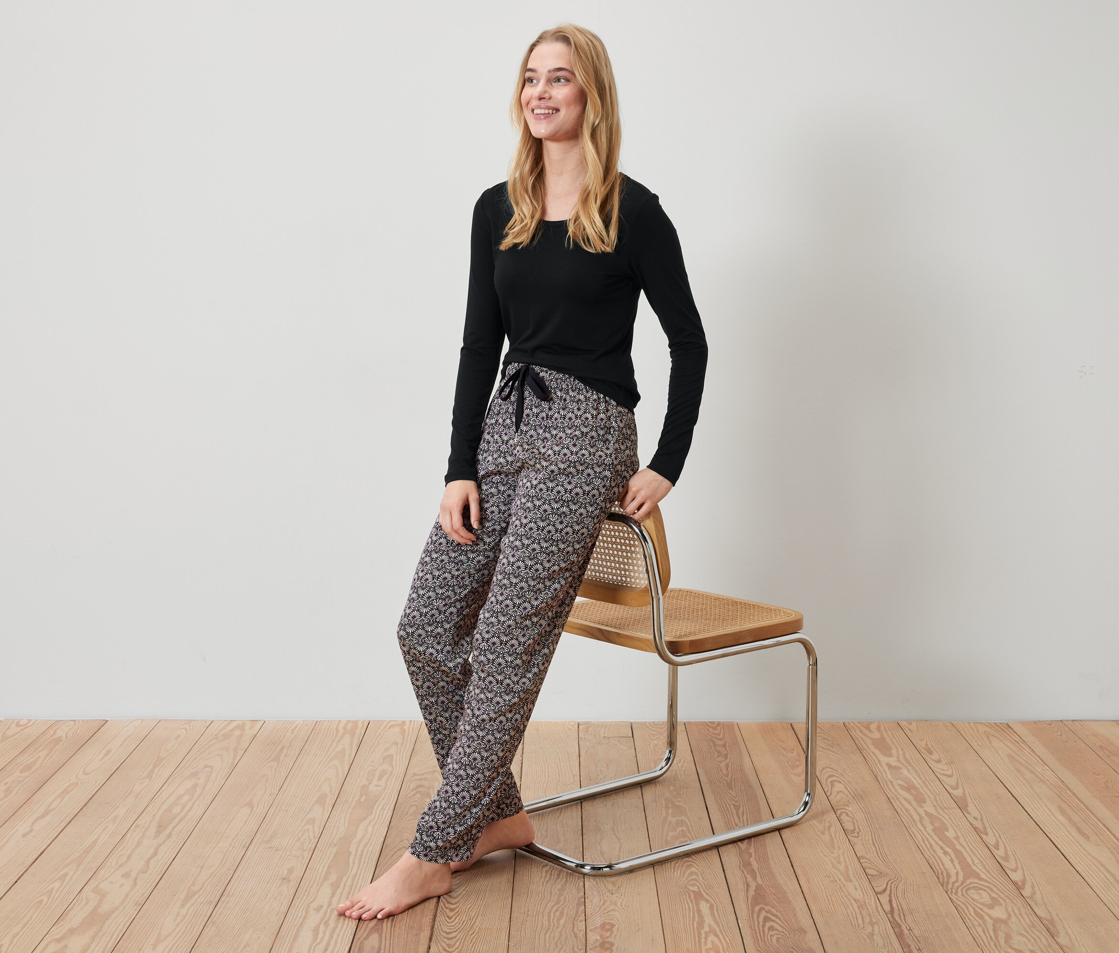 Siyah bluzlu ve desenli pantolonlu sarışın bir kadın sandalyeye yaslanmış.