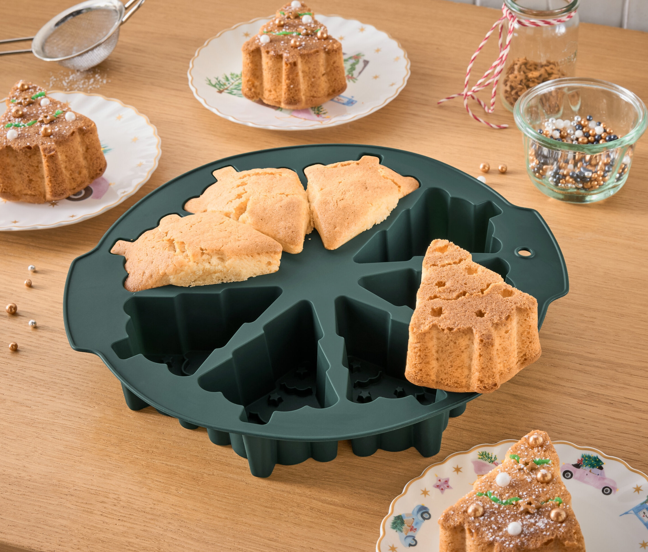 Noel ağacı şeklinde pişirme kalıbı, pişmiş kekler ve tabaklarda süslenmiş kekler ile birlikte duruyor.