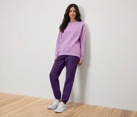 Bir kadın lila sweatshirt ve mor eşofmanla poz veriyor.