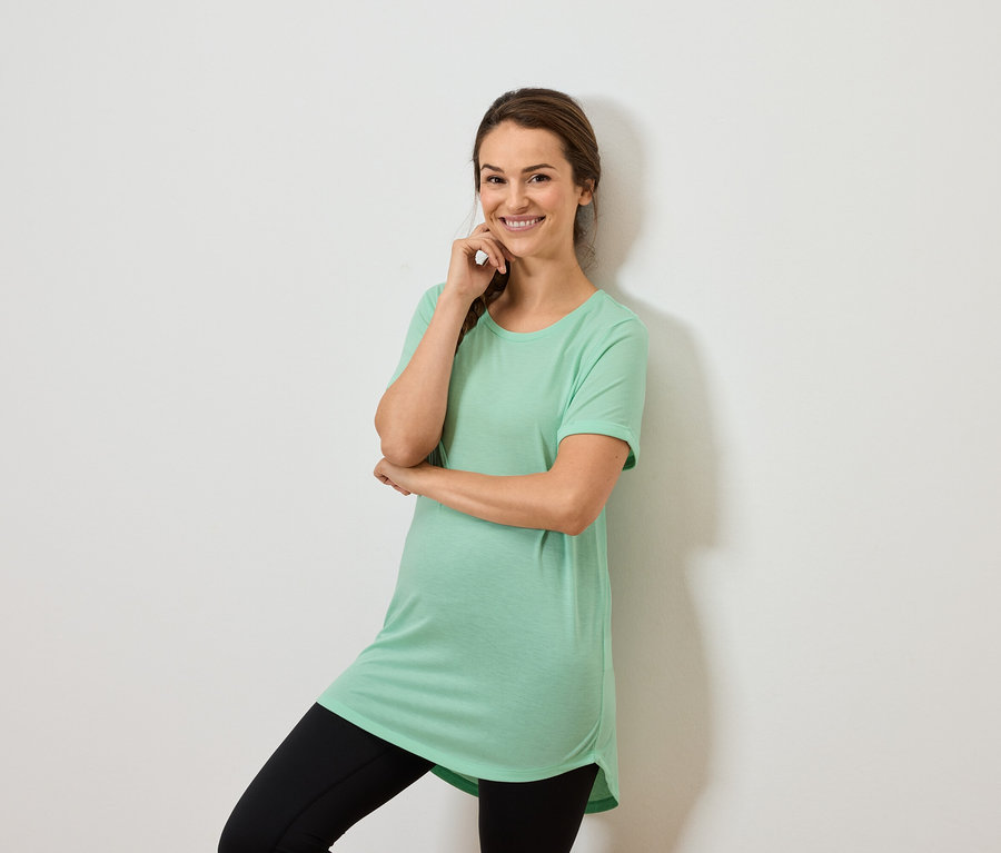 Nane yeşili bir üst ve siyah tayt giyen bir kadın çenesi üzerinde eliyle poz veriyor.