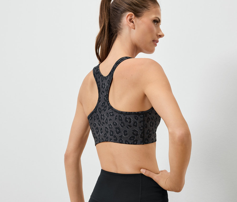 Sırtı kameraya dönük bir kadın, hayvan desenli bir sporcu sütyeni ve siyah tayt giyiyor.