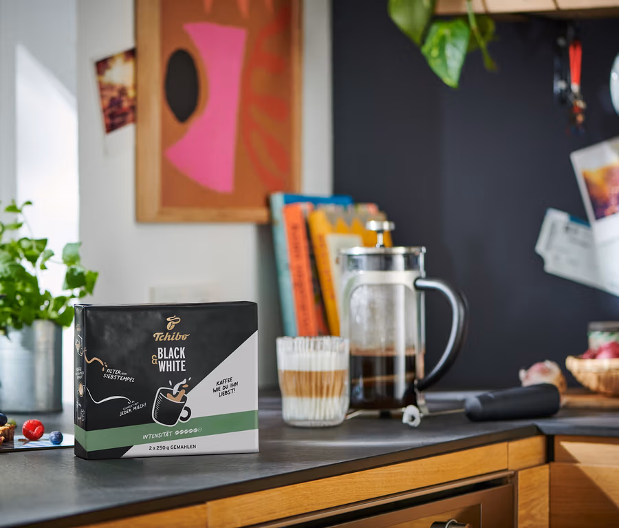 Mutfak tezgahında bir paket BLACK & WHITE - 2 x 250 g öğütülmüş kahve, bir French press ve bir bardak kahve duruyor.