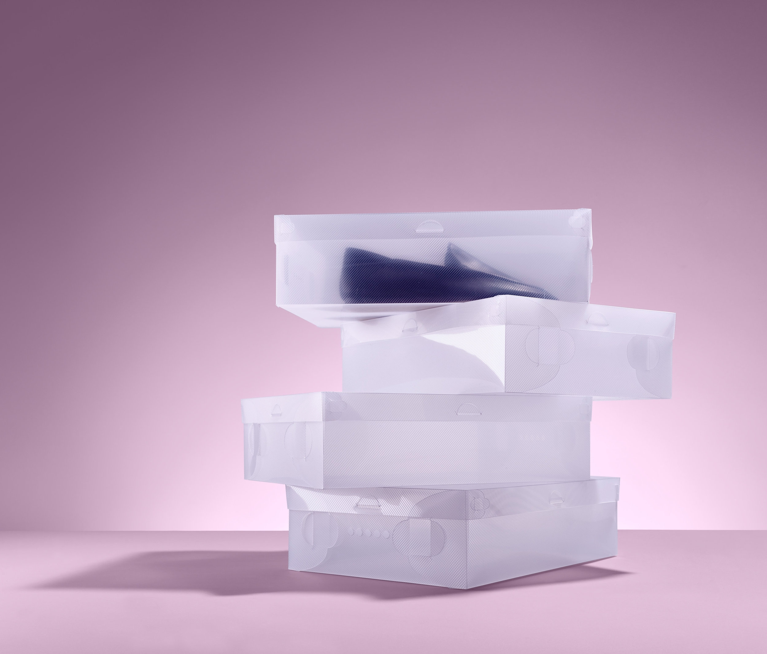 Pembe bir arka plan üzerinde üst üste yığılmış dört adet ayakkabı saklama kutusu.