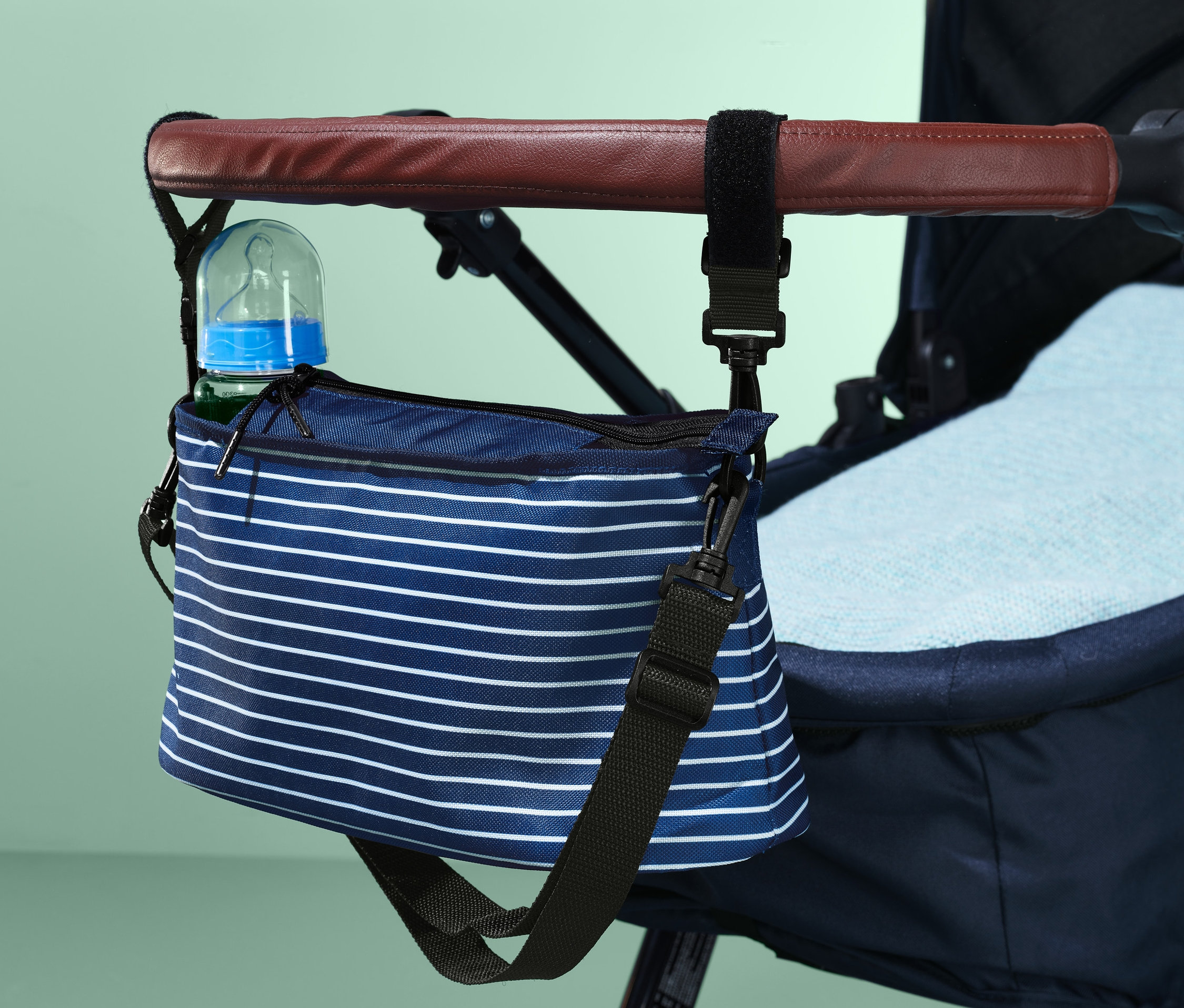 Biberonlu, bebek arabasının koluna takılmış mavi beyaz çizgili bebek arabası çantası.