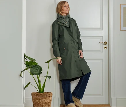 Kapüşonlu yeşil renkli 2'si 1 Arada Outdoor Parka giyen kadın kapıya yaslanmış.