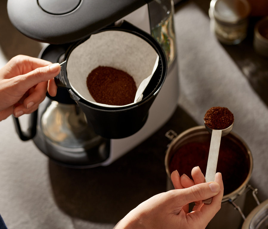 Kadın, beyaz »Let's Brew« filtre kahve makinesine kahve ekliyor.