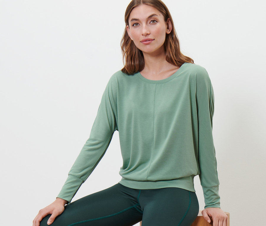 Kadın ahşap blokların üzerinde oturuyor, ada çayı yeşili renginde spor ve yoga üstü giyiyor.