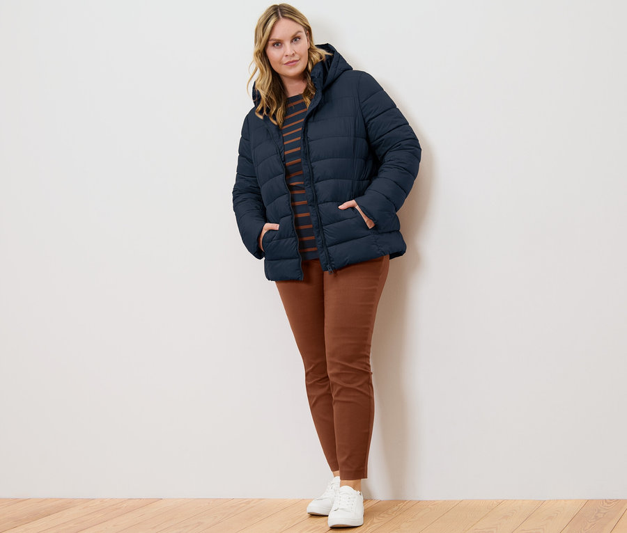 Kadın lacivert kapüşonlu kapitone mont, çizgili 3/4 kollu tişört ve konyak rengi streç pantolonla poz veriyor.